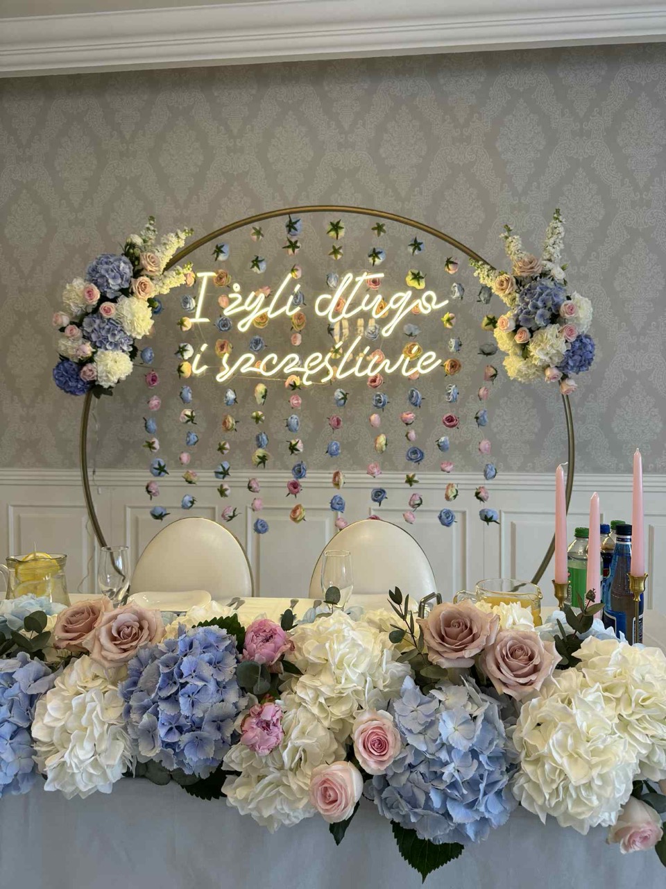 Klasyczny neon ślubny "I żyli długo i szczęśliwie" dopasowany do złotej obręczy. Dekoracja LED dostępna w sprzedaży hurtowej i ofercie wynajmu.